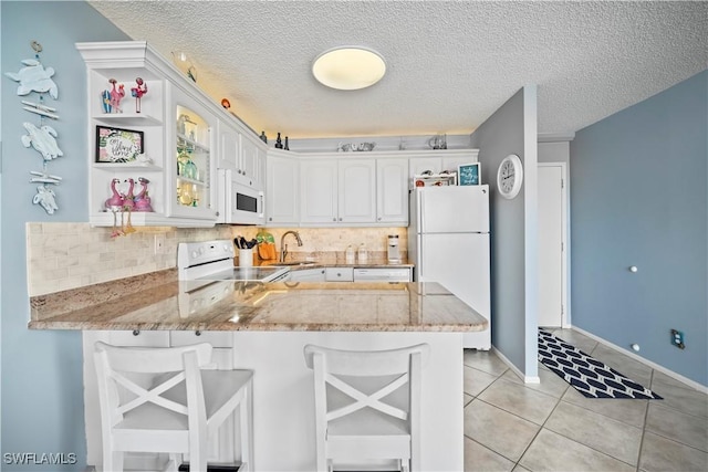 kitchen featuring light stone counters, a peninsula, white appliances, white cabinets, and tasteful backsplash