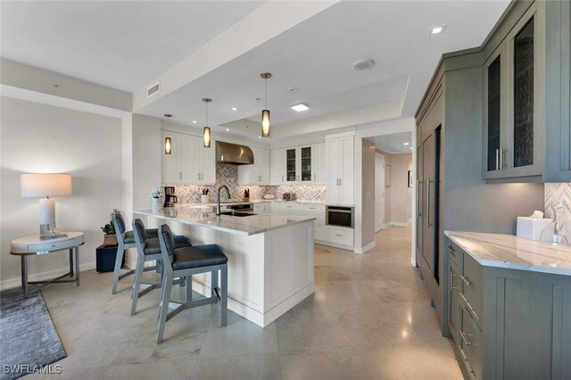 kitchen featuring pendant lighting, wall chimney range hood, white cabinetry, a kitchen bar, and kitchen peninsula