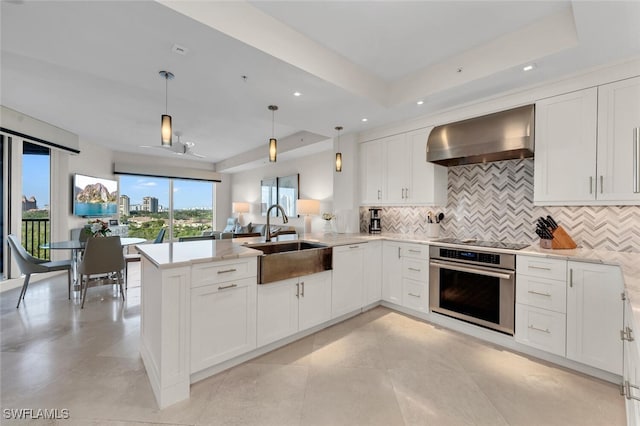 kitchen with wall chimney exhaust hood, oven, sink, and kitchen peninsula