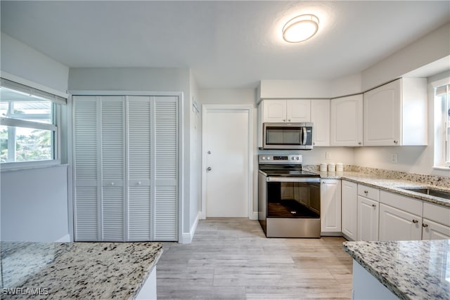 kitchen with sink, light wood-type flooring, light stone countertops, appliances with stainless steel finishes, and white cabinets