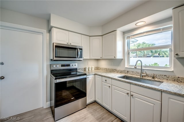 kitchen with appliances with stainless steel finishes, white cabinets, light stone countertops, light hardwood / wood-style flooring, and sink