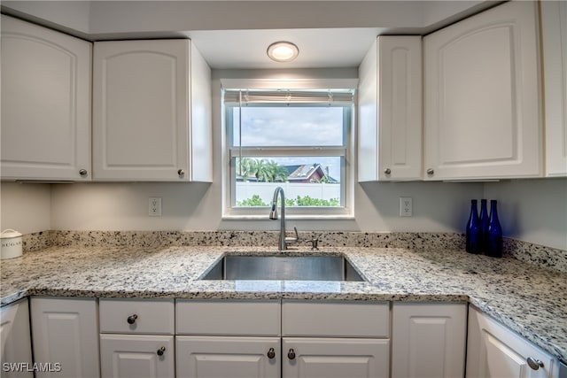 kitchen with sink, light stone counters, and white cabinetry