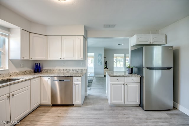 kitchen with stainless steel appliances, light stone countertops, white cabinets, and light hardwood / wood-style floors