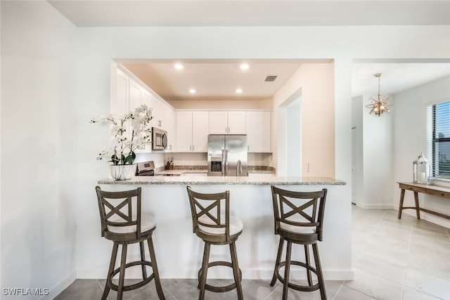 kitchen with stainless steel appliances, light stone countertops, kitchen peninsula, and white cabinets