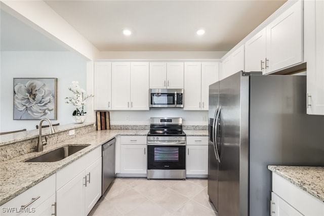 kitchen featuring appliances with stainless steel finishes, white cabinetry, sink, light tile patterned floors, and light stone countertops