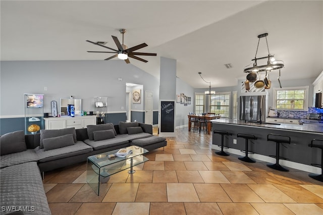 living room featuring sink, lofted ceiling, ceiling fan with notable chandelier, and light tile patterned floors