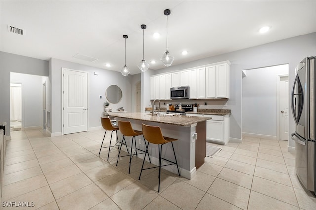 kitchen featuring stainless steel appliances, a kitchen island with sink, hanging light fixtures, light stone countertops, and white cabinets