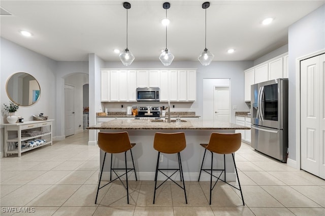 kitchen with light stone countertops, stainless steel appliances, white cabinetry, and a kitchen island with sink