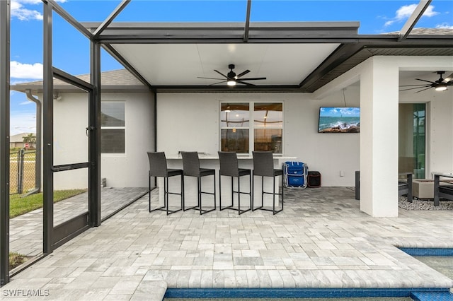 view of patio / terrace featuring ceiling fan, glass enclosure, and an outdoor bar