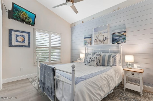 bedroom featuring ceiling fan, vaulted ceiling, wooden walls, and hardwood / wood-style flooring