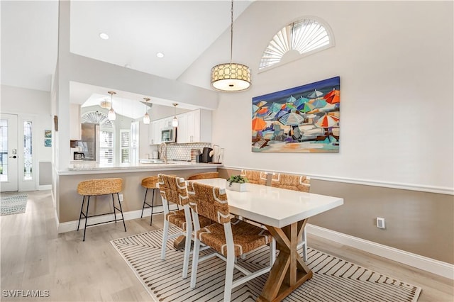 dining room with high vaulted ceiling, sink, and light wood-type flooring