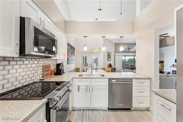 kitchen with pendant lighting, sink, light stone countertops, appliances with stainless steel finishes, and white cabinets