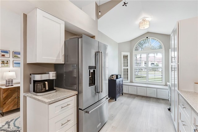 kitchen featuring lofted ceiling, high quality fridge, light wood-type flooring, light stone countertops, and white cabinets