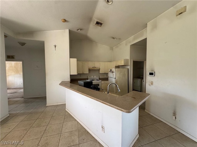 kitchen featuring light tile patterned floors, under cabinet range hood, white appliances, cream cabinetry, and washer / clothes dryer