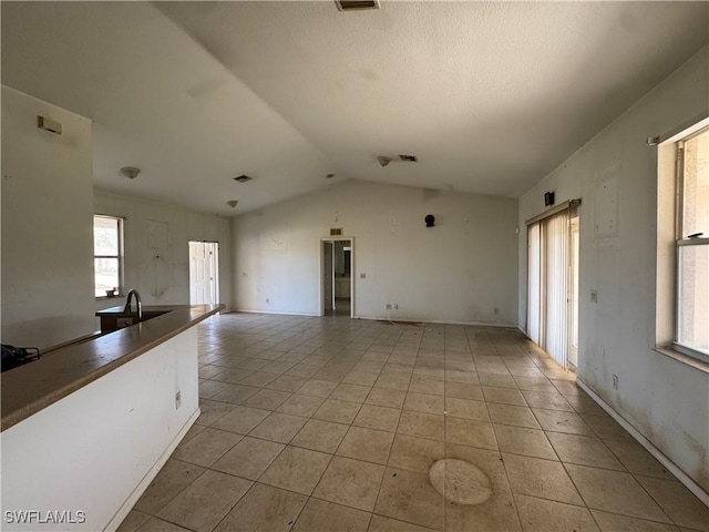 unfurnished living room with lofted ceiling, a textured ceiling, and light tile patterned flooring