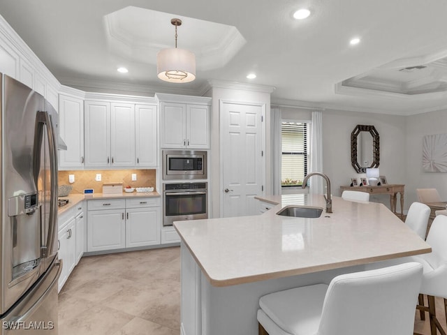 kitchen with stainless steel appliances, a kitchen island with sink, white cabinets, and a tray ceiling