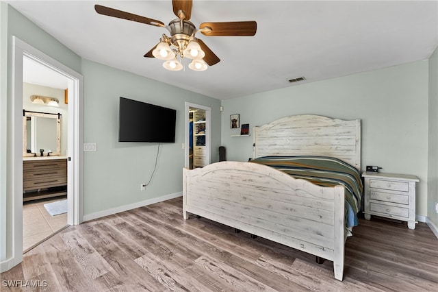 bedroom featuring ceiling fan, hardwood / wood-style flooring, ensuite bath, a walk in closet, and a closet