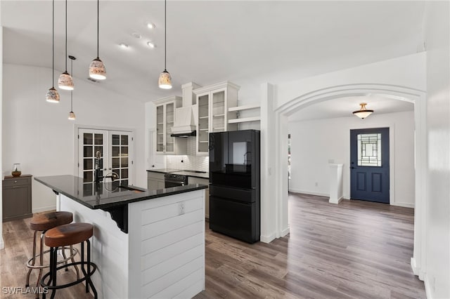 kitchen featuring a kitchen bar, white cabinetry, an island with sink, backsplash, and black fridge