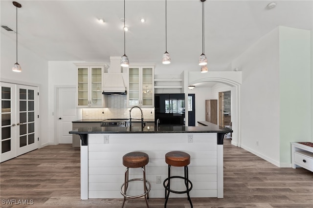 kitchen with a kitchen bar, white cabinetry, french doors, an island with sink, and decorative backsplash