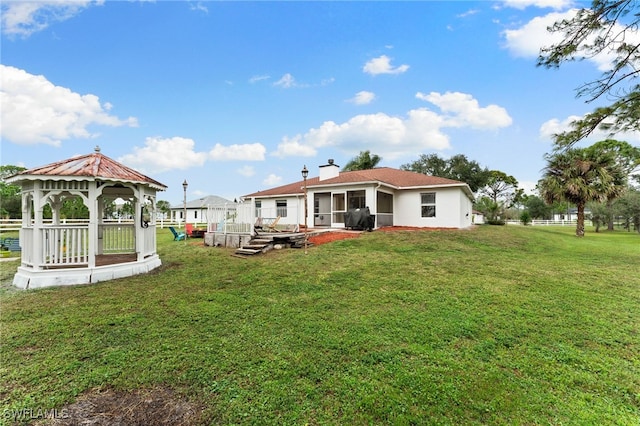 rear view of house featuring a lawn, a sunroom, a gazebo, and a deck