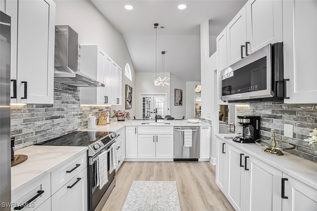 kitchen featuring wall chimney range hood, white cabinetry, hanging light fixtures, stainless steel appliances, and light stone counters