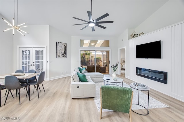 living room with vaulted ceiling, ceiling fan with notable chandelier, french doors, and light wood-type flooring