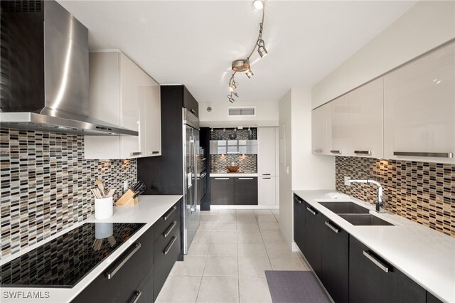 kitchen with modern cabinets, a sink, decorative backsplash, dark cabinetry, and wall chimney range hood