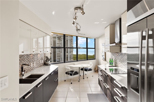kitchen featuring wall chimney range hood, decorative backsplash, a sink, stainless steel refrigerator with ice dispenser, and modern cabinets