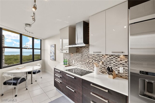 kitchen featuring stainless steel built in fridge, white cabinetry, wall chimney exhaust hood, black electric cooktop, and dark brown cabinetry