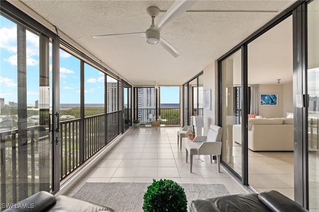 sunroom with a textured ceiling, ceiling fan, expansive windows, and tile patterned floors