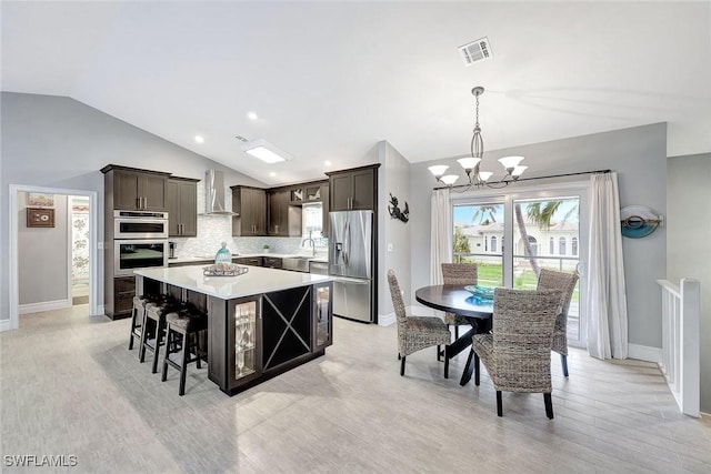 kitchen with lofted ceiling, stainless steel appliances, a center island, tasteful backsplash, and wall chimney exhaust hood