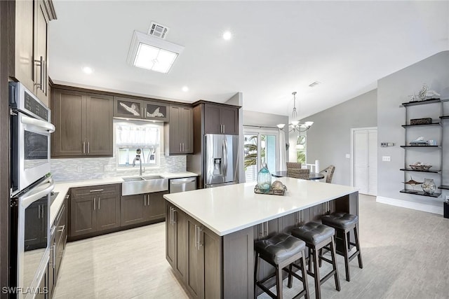 kitchen with vaulted ceiling, a kitchen island, decorative light fixtures, backsplash, and stainless steel appliances