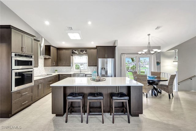 kitchen with wall chimney range hood, sink, appliances with stainless steel finishes, a kitchen island, and vaulted ceiling