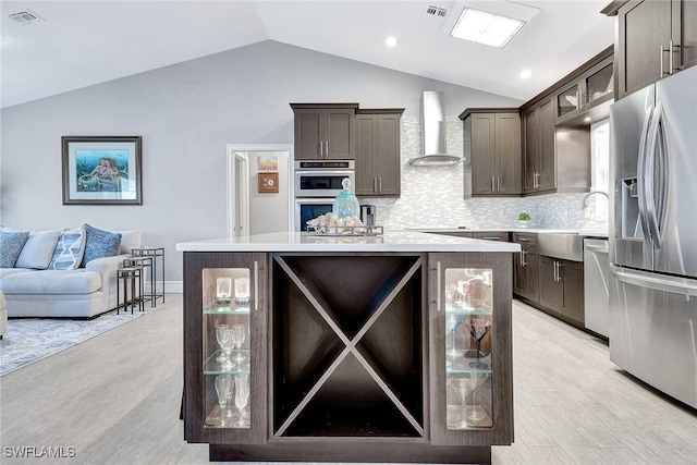 kitchen with wall chimney range hood, vaulted ceiling, stainless steel appliances, and a kitchen island