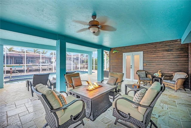 view of patio featuring french doors, glass enclosure, ceiling fan, and a fire pit