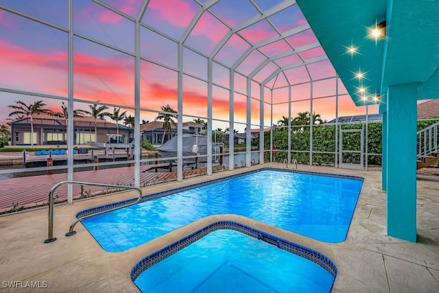 pool at dusk with an in ground hot tub, glass enclosure, and a patio area