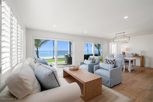 living room with a water view, plenty of natural light, an inviting chandelier, and light hardwood / wood-style floors