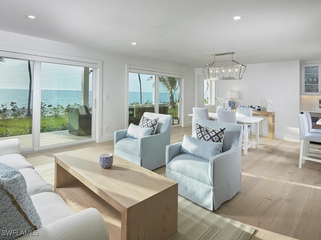 living room with light wood-type flooring, a chandelier, and a water view