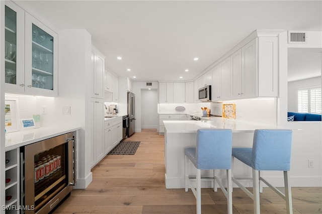 kitchen with appliances with stainless steel finishes, wine cooler, white cabinets, a kitchen bar, and kitchen peninsula