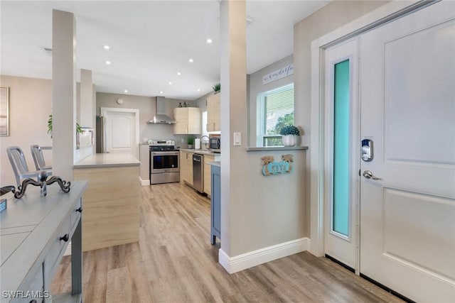 kitchen with wall chimney range hood, light hardwood / wood-style flooring, and appliances with stainless steel finishes