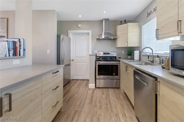 kitchen featuring sink, light brown cabinets, stainless steel appliances, wall chimney range hood, and light hardwood / wood-style flooring