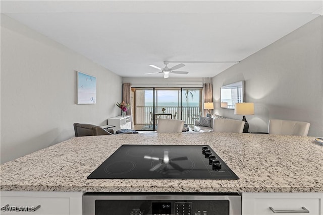 kitchen featuring light stone countertops, white cabinets, oven, ceiling fan, and black electric cooktop