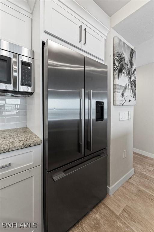 kitchen with light stone countertops, white cabinets, appliances with stainless steel finishes, and light hardwood / wood-style flooring