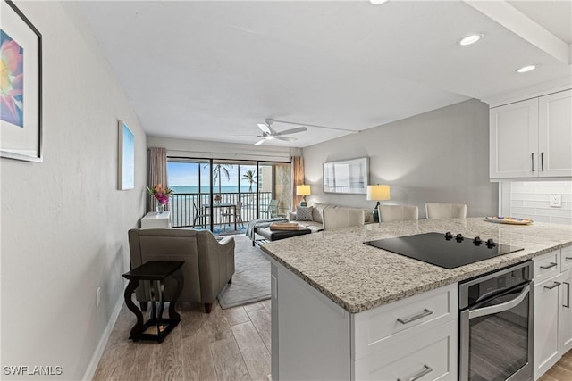 kitchen with light stone countertops, black electric stovetop, white cabinetry, and oven