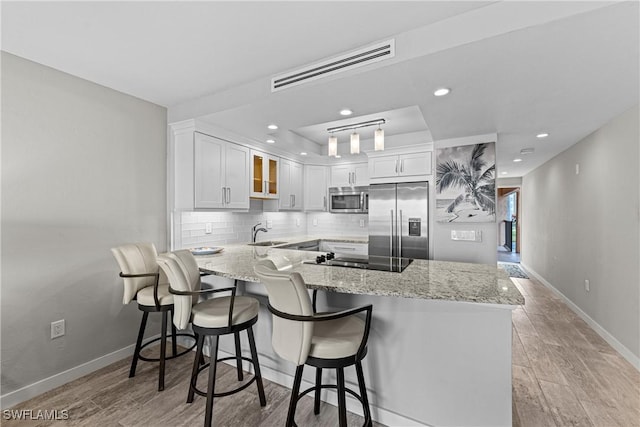 kitchen with white cabinetry, kitchen peninsula, appliances with stainless steel finishes, light stone counters, and sink