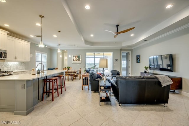 living room featuring ceiling fan, ornamental molding, plenty of natural light, and a tray ceiling