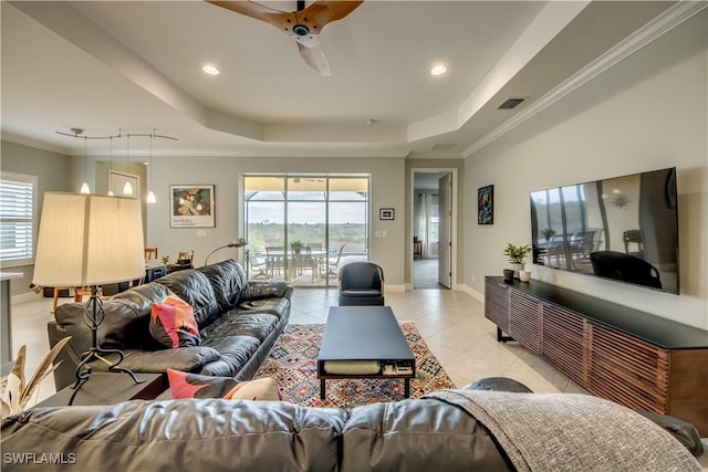 tiled living room with ceiling fan, a tray ceiling, and ornamental molding