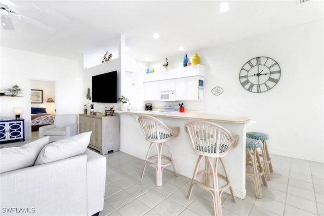 kitchen featuring a breakfast bar area, kitchen peninsula, light tile patterned flooring, and white cabinetry