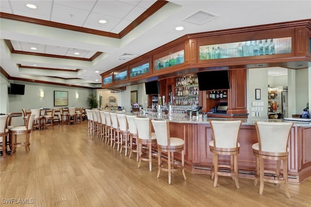 bar featuring light wood-type flooring, ornamental molding, and light stone countertops