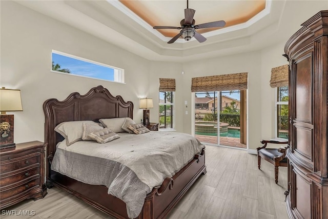 bedroom with a towering ceiling, access to exterior, ceiling fan, a tray ceiling, and light hardwood / wood-style flooring